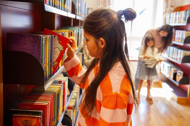 Ein Mädchen zieht ein Buch aus einem Buecherregal