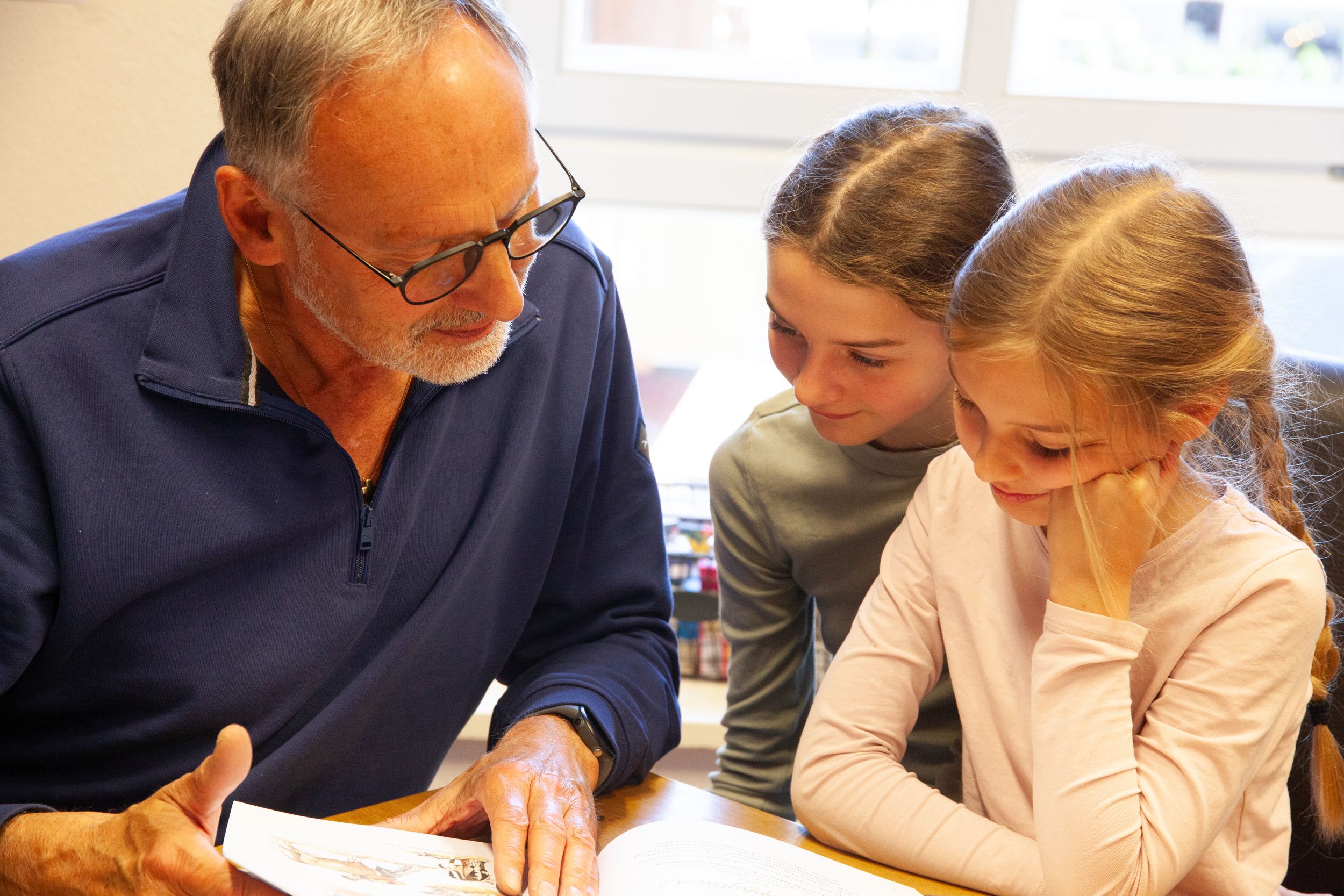 Älterer Herr liest mit Enkelkindern in einem Buch