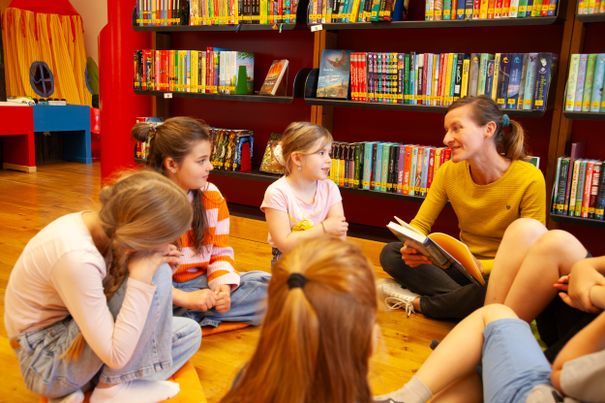 Büchereimitarbeiterin mit Kindern und Jugendlichen beim gemeinsamen Lesen eines Buches