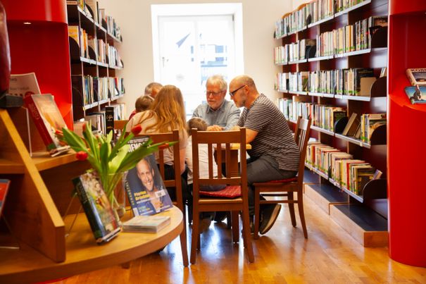 Spieler sitzen am Spieltisch zwischen Bücherregalen in der Buecherei Grassau