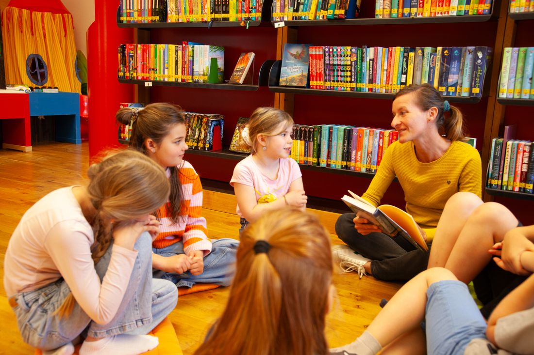 Büchereimitarbeiterin mit Kindern und Jugendlichen beim gemeinsamen Lesen eines Buches